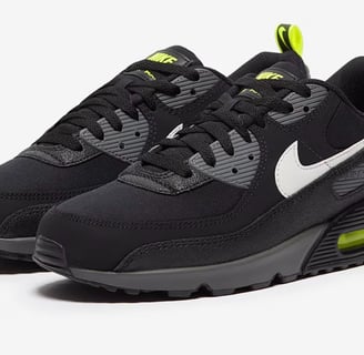 Nike Air Max 90 sneakers in black with neon yellow accents, visible Air cushioning, and mesh upper