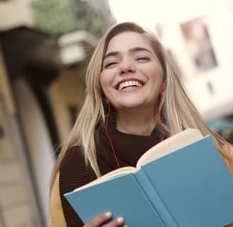 a woman in a brown sweater and earphones is smiling and holding a book
