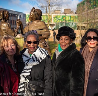 a group of women standing in front of a statue of a man