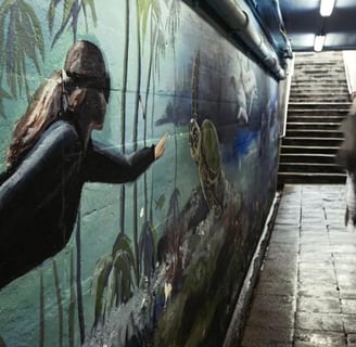 Blurred figures passing a painted underwater mural in a dimly lit pedestrian tunnel