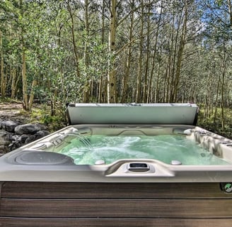 Hot tub with open lid and bubbling water in a forested backyard
