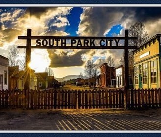 Wooden gate marked "South Park City" leading into a historic western town replica at sunset.
