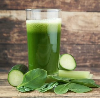 a glass of green juice with a slice of cucumber on the side