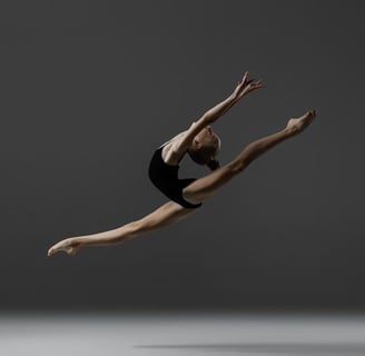 A young graceful rhythmic gymnast performing a split leap in the air.
