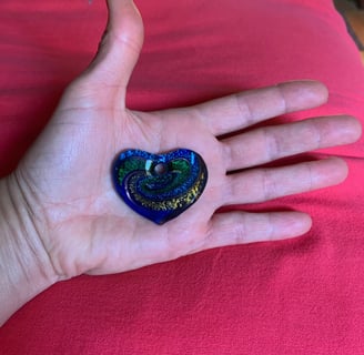 open hand with blue green 7 yellow glass heart on palm