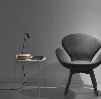 Lámpara de sobremesa con base circular junto a butaca en ambiente de lectura moderno