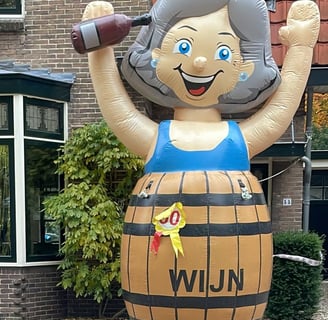 Opblaas pop Sarah met blauwe jurk in bruin wijnvat aan de voorkant van een huis