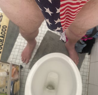 a man wearing a g-string that has a USA flag pattern while standing in front of a toilet
