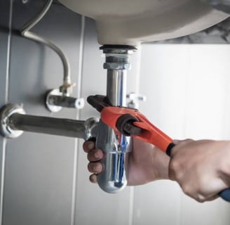 man using a mini pipe wrench to turn a pipe under a sink