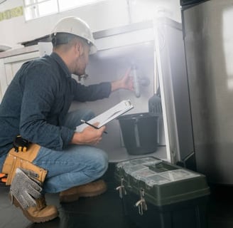 plumber inspecting a pipe under a sink wearing a hard hat