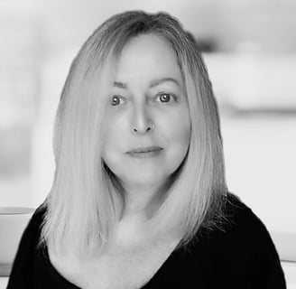 A black and white mid shot of a middle aged woman with long blonde hair and a nose ring.