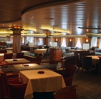Restaurante elegante a bordo de navio de cruzeiro, com mesas arrumadas, iluminação suave.
