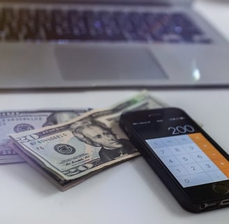 U.S. $10 and $20 dollar bills with a calculator app displayed on an iPhone next to it.