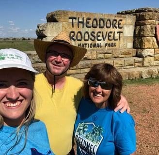 a man and two women standing in front of a sign that says theodore roosevelt national park