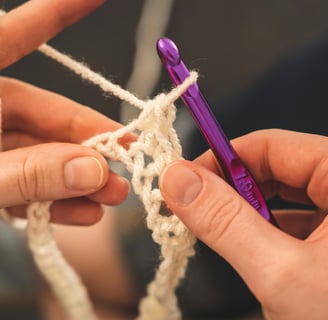 Des mains utilise un crochet de couleur violet pétant de taille de 7.0mm pour crocheter du fil
