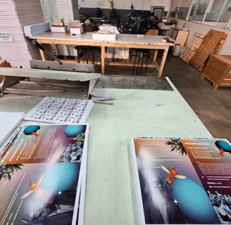 Impressos offset recém-saídos na mesa de corte da Editograf com pilhas de papel ao fundo.