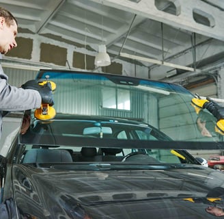 two workers lift a windshield into place