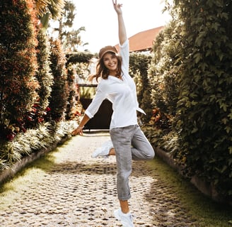 a woman in a white shirt and grey pants is doing a happy pose