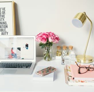 a laptop computer sitting on a desk with a vase of flowers