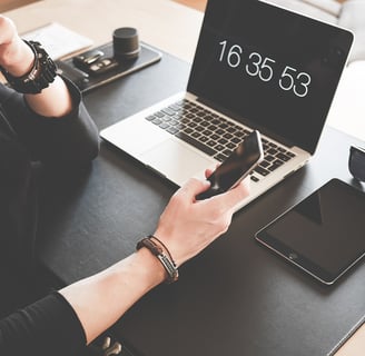 Elderly woman sitting at a desk with a laptop and a cell phone