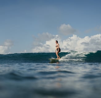 Woman taking surf lessons at a surf school in Kuta Lombok, riding a wave on a sunny ocean day