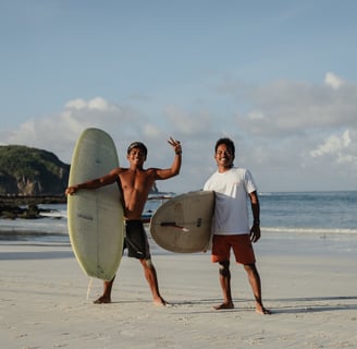 Two surf instructors at a surf school in Kuta Lombok holding boards on beach, offering surf lessons.