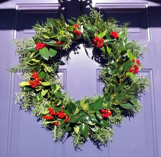 handmade rosemary holly berry and honeysuckle vine christmas wreath hanging on a sun-lit purple fron
