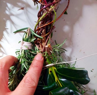 honeysuckle vine wreath and finger pointing to place rosemary bundle after cut ends of last bundle