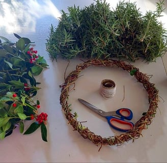 rosemary and holly berry bush cuttings beside a honeysuckle wreath base with scissors and twine on a