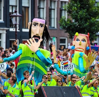 2 Giant puppets wearing yellow reflector vests used in the Amsterdam Pride one is covering mouth