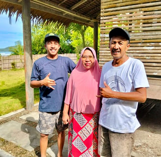 Owners of Afulu Surf Resort smiling on the beach with surf in the background.