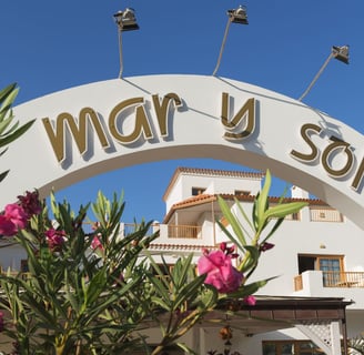 entrada del hotel mar y sol con arco blanco y escrita color oro