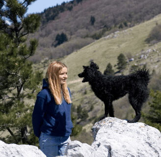 Jeune femme parlant à un chien noir devant des montagnes, symbolisant la communication animale.