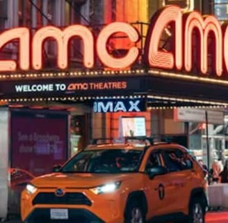 AMC entertainment holdings inc logo on top of theatre with orange taxi cab parked in front