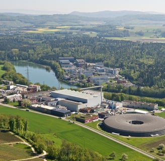 Aerial view of Paul Scherrer Institute complex with verdant landscape, lake, and forested hills