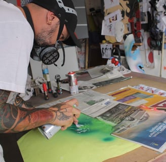 Detalhe das mãos do artista enquanto ajusta spray e tintas sobre a mesa de trabalho.