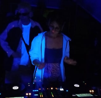 a woman in a white shirt and a man behind a DJ pult