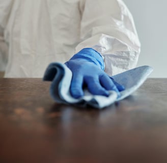 a person in a white lab coat and gloves cleaning a table