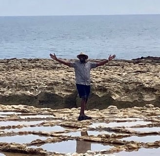 A man stands on the sea shore with his arms out wide. 