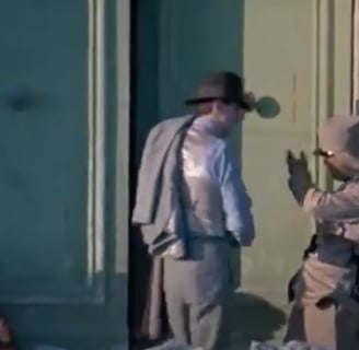 A man in a hat talks to a solider outside a building. 