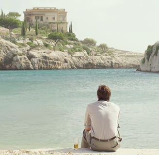 A man sitting on the beach overlooking a body of water.