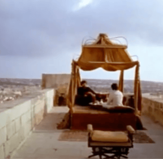 Two men sit under an elaborate canopy, overlooking a city.