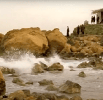 A group of people standing on rocks near a body of water.