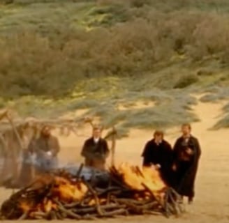 A group of people standing around a bonfire on a beach.