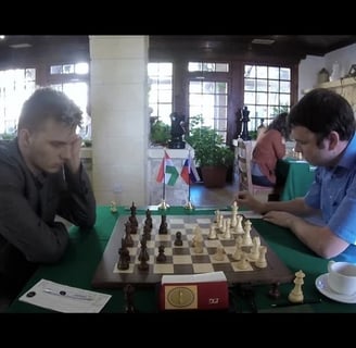 two men playing chess in a room with people.