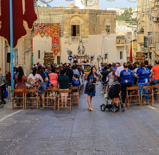 People sitting in a narrow street in front of a statue of St Mary.