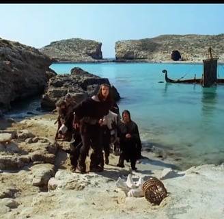 Group of men standing on a beach, in front of a half sunken ship.