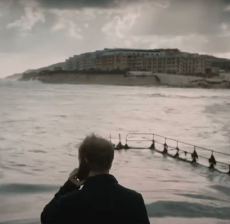 A man stands by a harbour, looking out to sea.