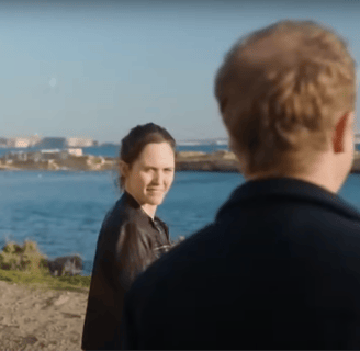 A man and woman stand looking at the sea.