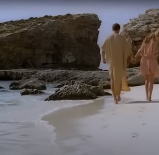 A man and woman walk along a beach.